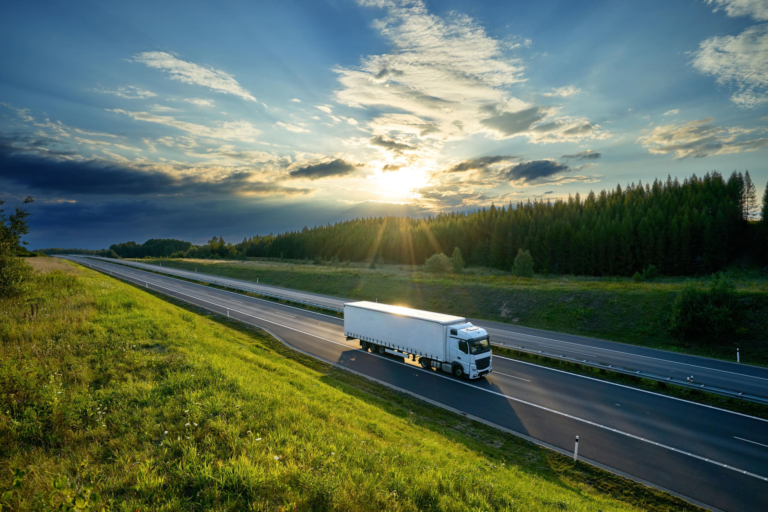 Semi truck driving down a highway at sunset